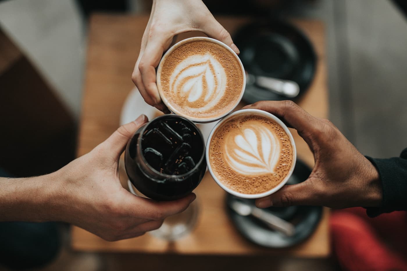Three hands holding coffee drinks with latte art